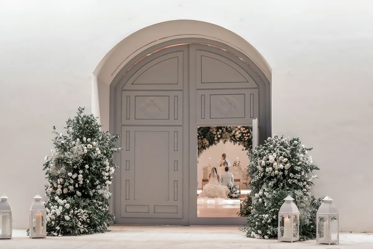 Ceremonia de matrimonio católico vista desde la puerta de la capilla, decorada con flores blancas