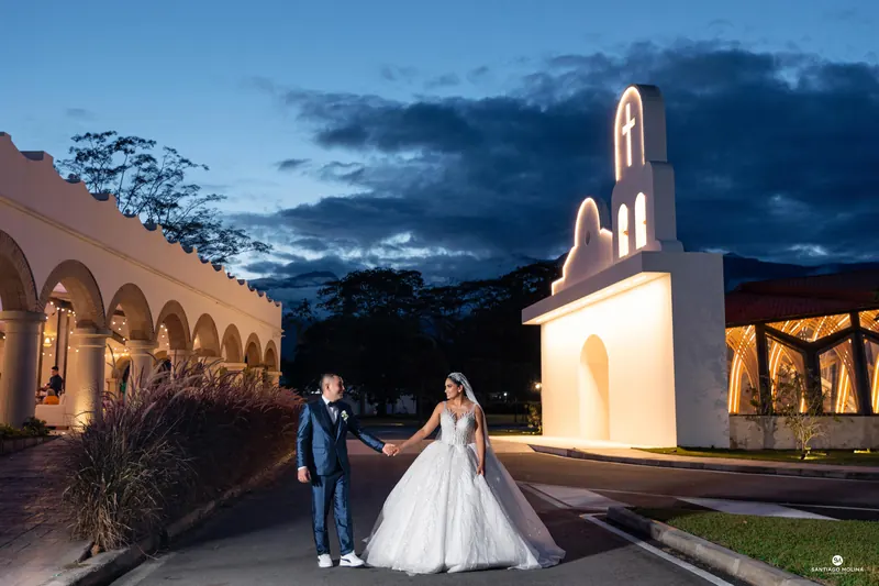 Novios tomados de la mano frente a la capilla iluminada en su boda en Villavicencio