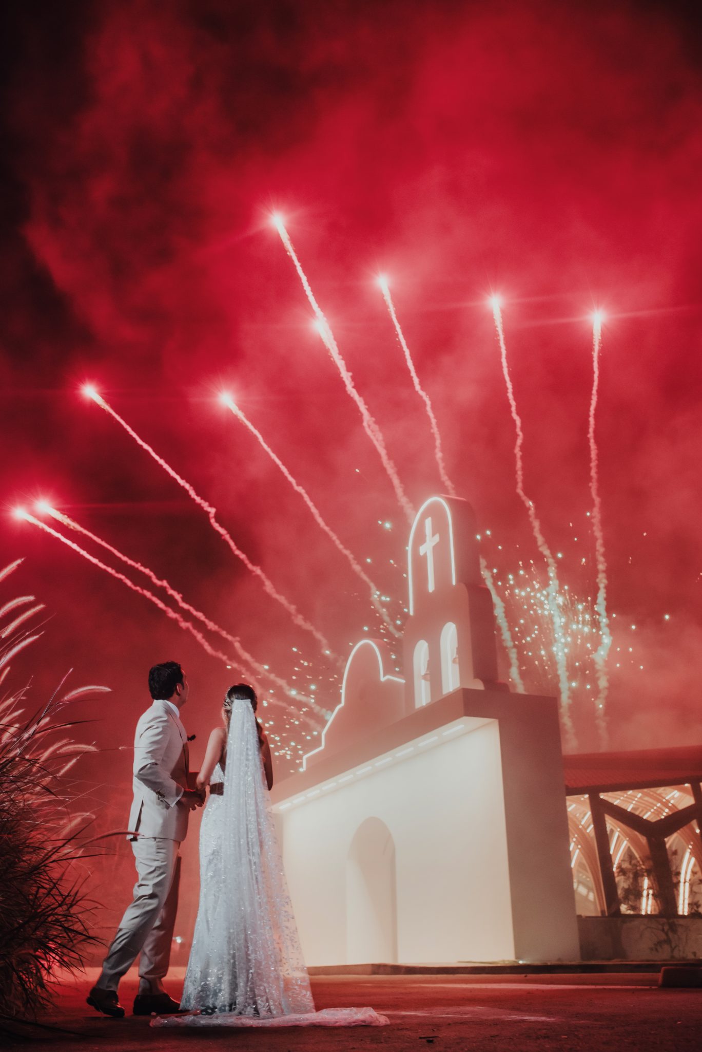 Novios con fuegos artificiales rojos sobre la capilla