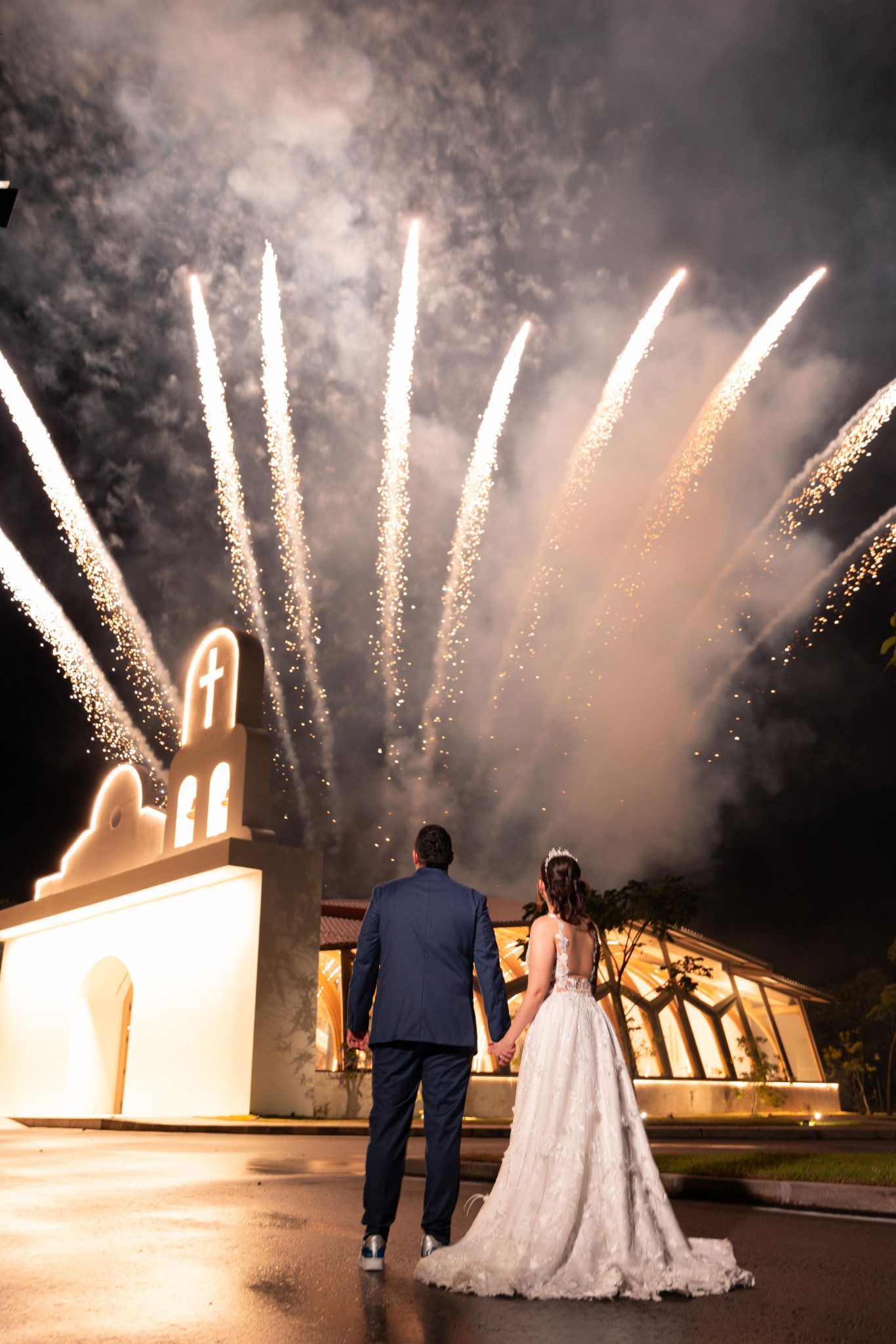 Novios con fuegos artificiales dorados frente a la capilla